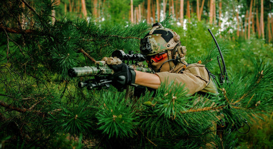 Airsoft Canada player in full tactical gear aiming a camouflaged airsoft sniper rifle in a dense forest environment.